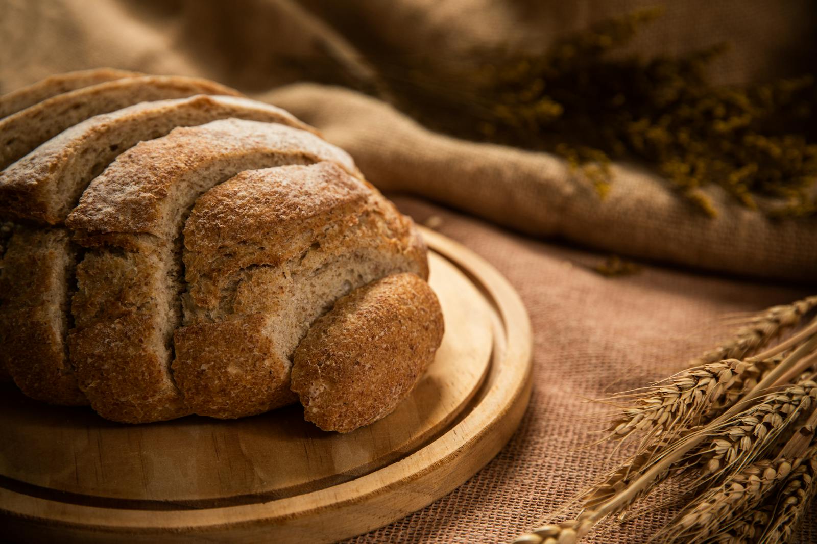 Freshly baked whole wheat bread loaf on a wooden board with wheat stalks
