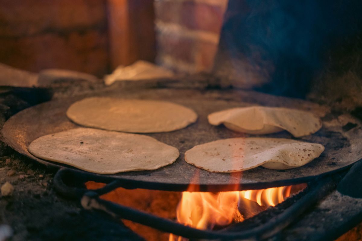 Round corn tortillas cooking on a traditional comal over an open flame.