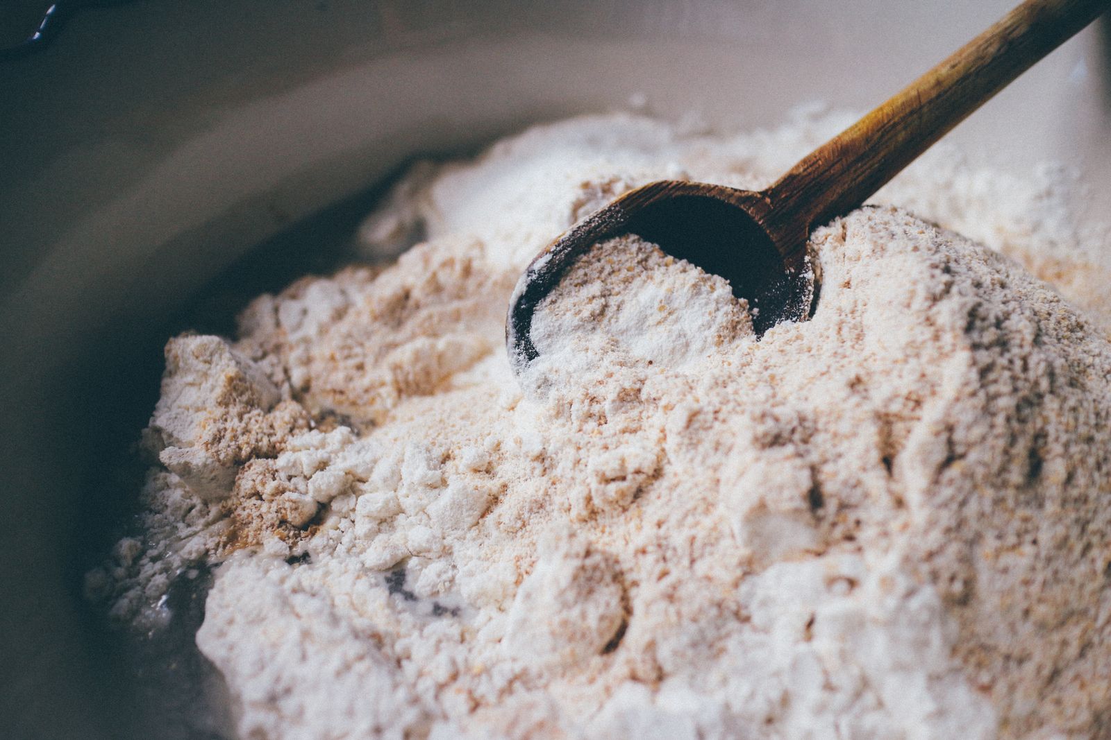 A wooden spoon resting in a mound of pale flour on a work surface