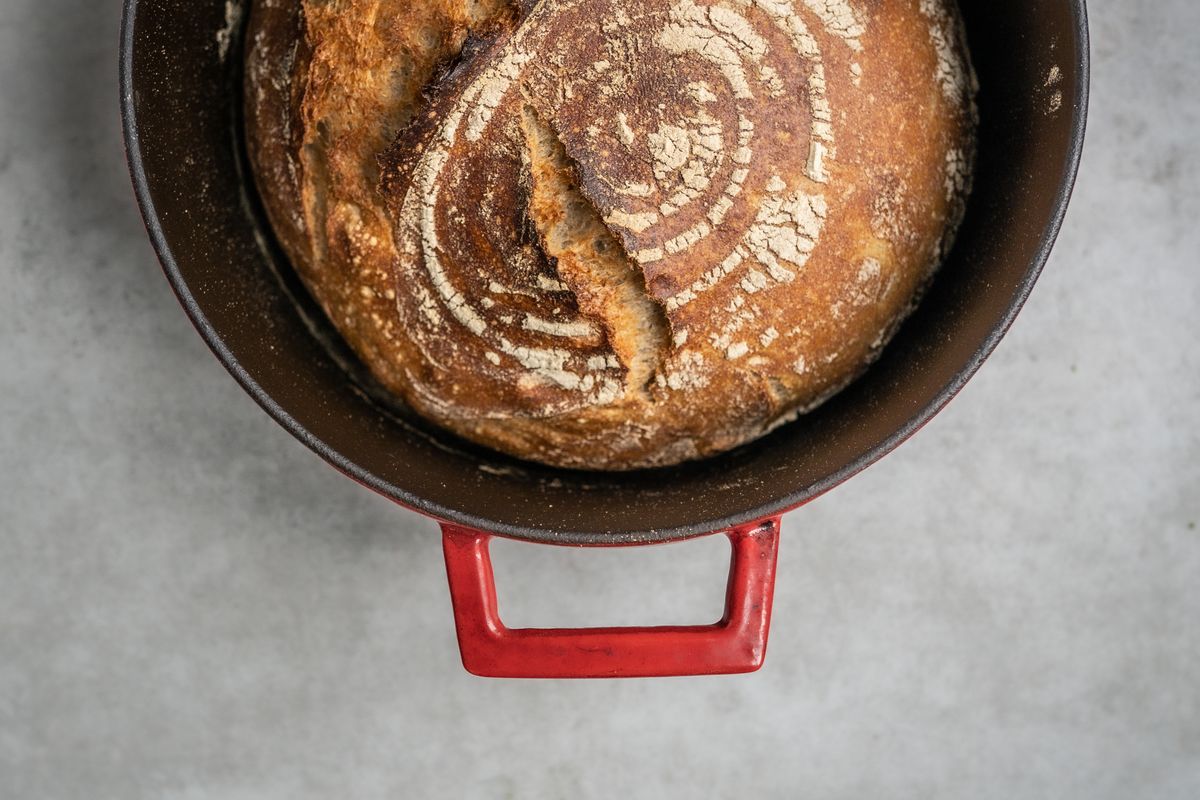 Freshly baked artisan bread with a rustic crackled crust sitting in a red Dutch oven.