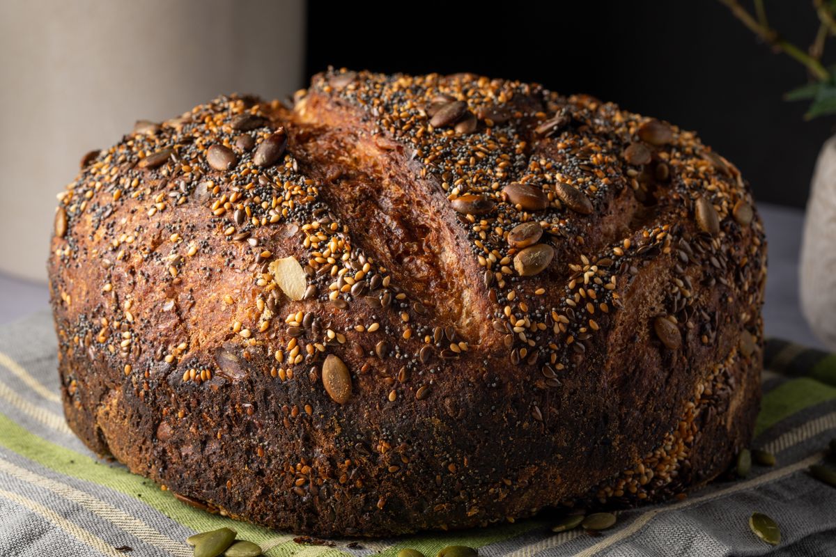 A dense, seeded whole-grain loaf on a board, the style a sprouted Ezekiel bread bakes into.