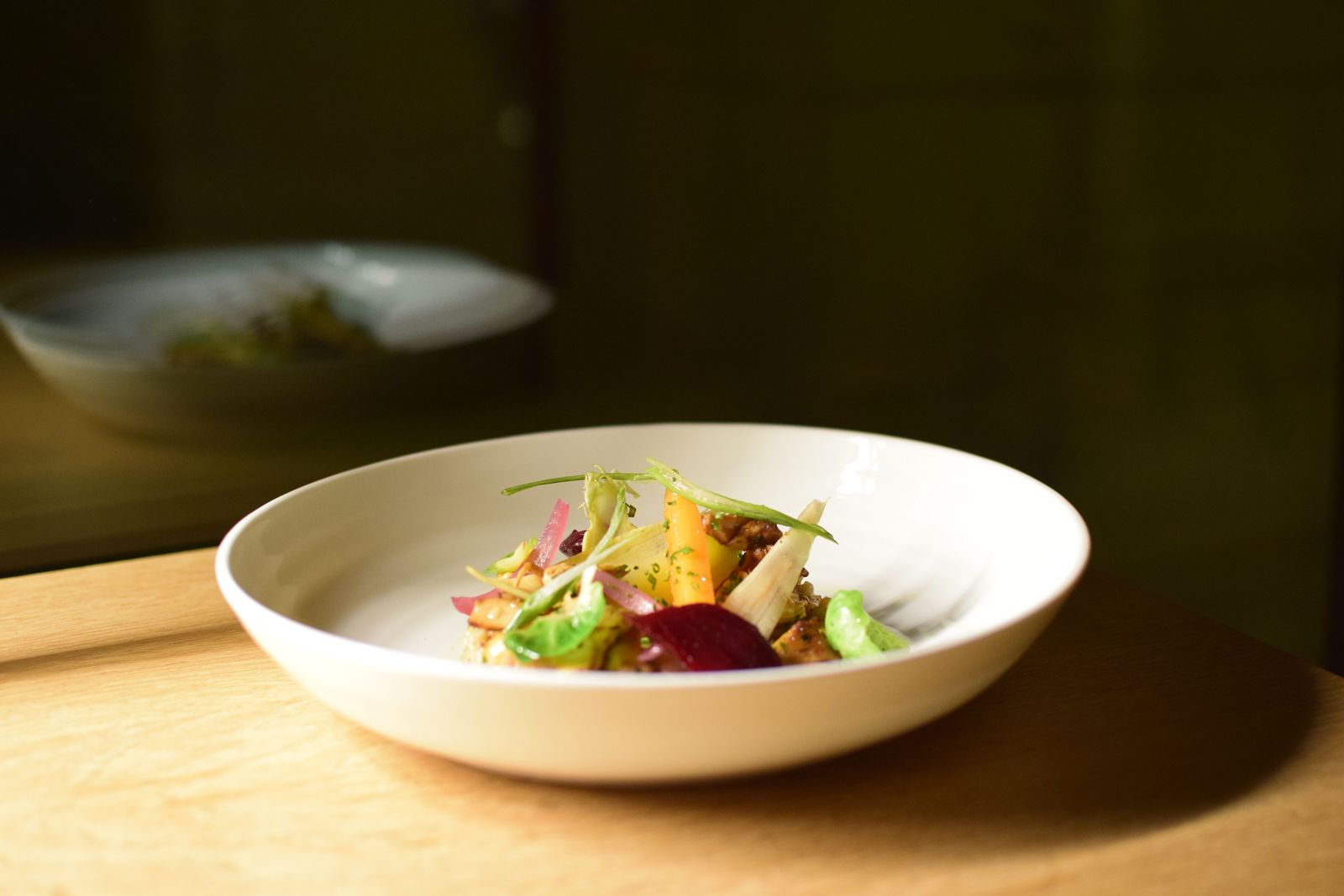 A plated grain salad with greens and vegetables in natural light on a wooden table