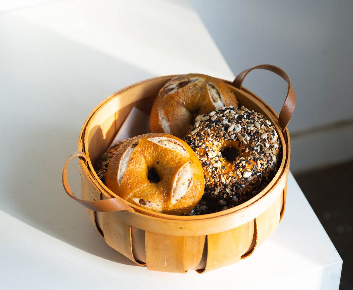 A selection of freshly baked bagels, including an everything bagel, in a rustic wooden basket.