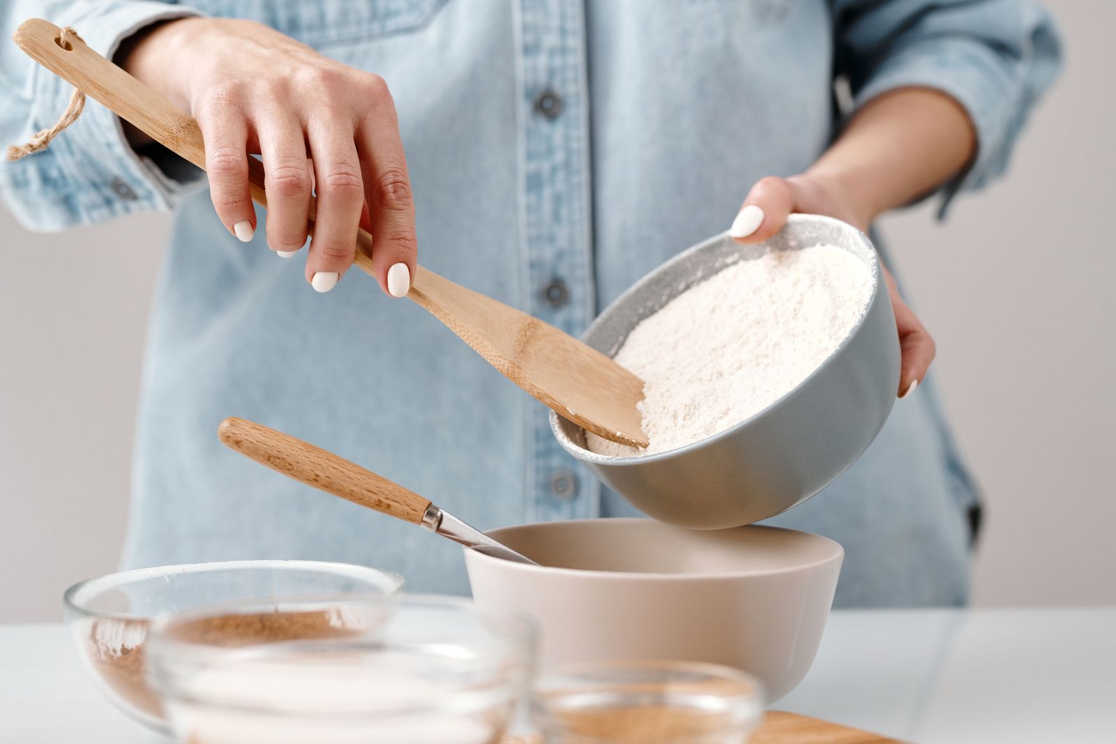 Hands adding flour to a mixing bowl on a kitchen counter