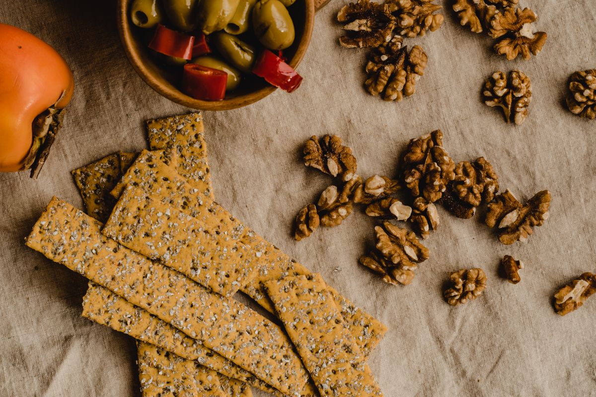 Flat lay of seeded crackers, walnuts, and olives arranged on a linen cloth.