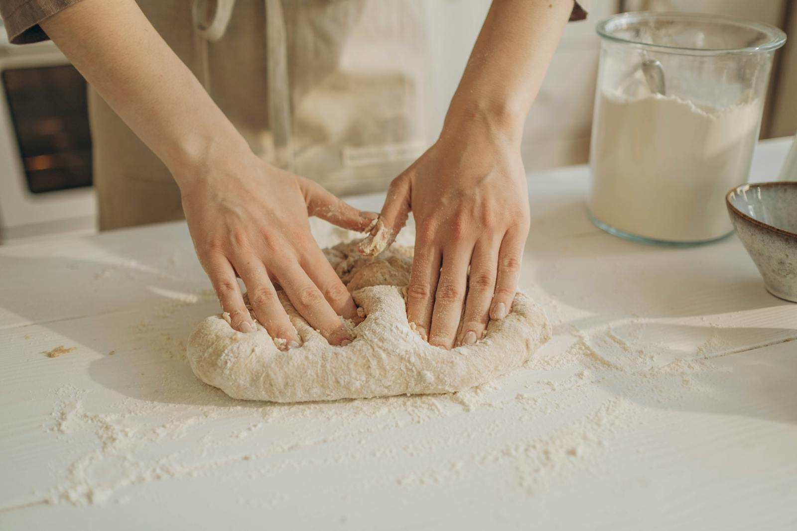 Hands kneading dough on a white table dusted with flour, the everyday baking scene at the heart of any gluten free flour decision.