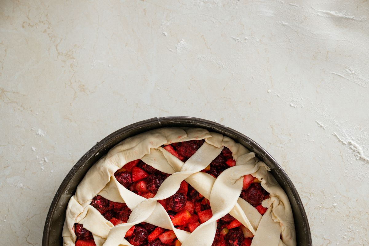 Overhead view of an unbaked cherry pie with a lattice crust on a floured surface.