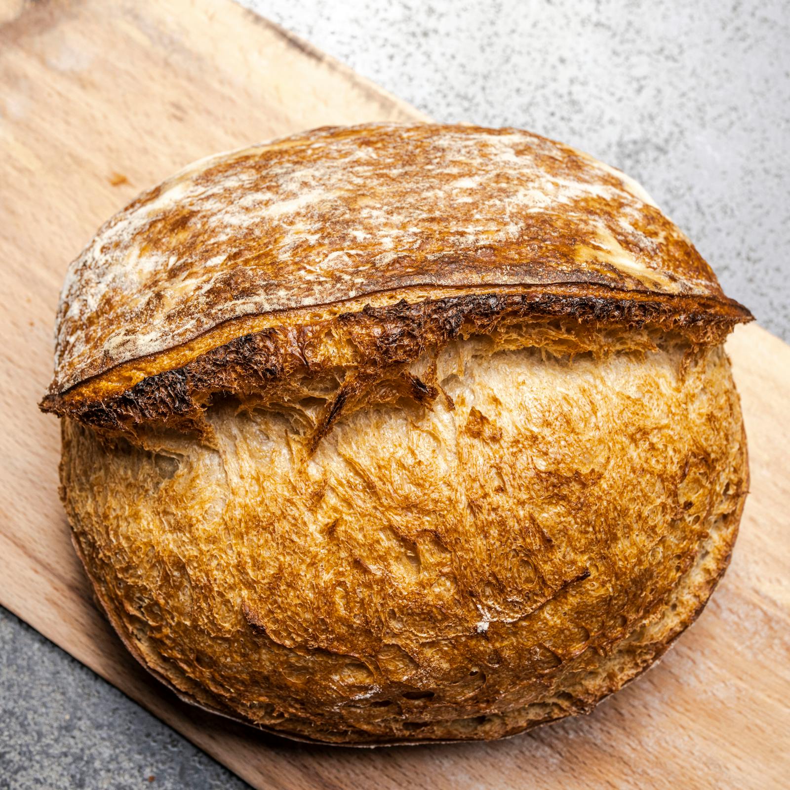 A round artisan sourdough loaf with a golden, crackled crust resting on a wooden board.