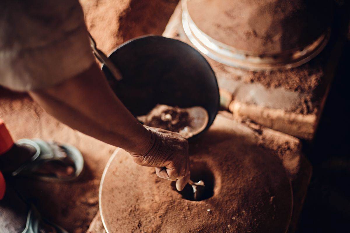 A hand turning a traditional stone grain mill indoors, grinding grain into flour.