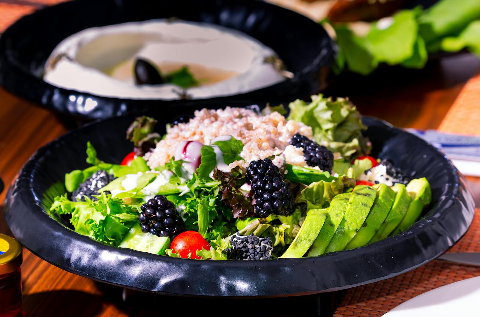 A grain salad bowl with cooked grains, avocado, lettuce, and blackberries in a black ceramic bowl, the kind of dish farro lives in once it is cooked.