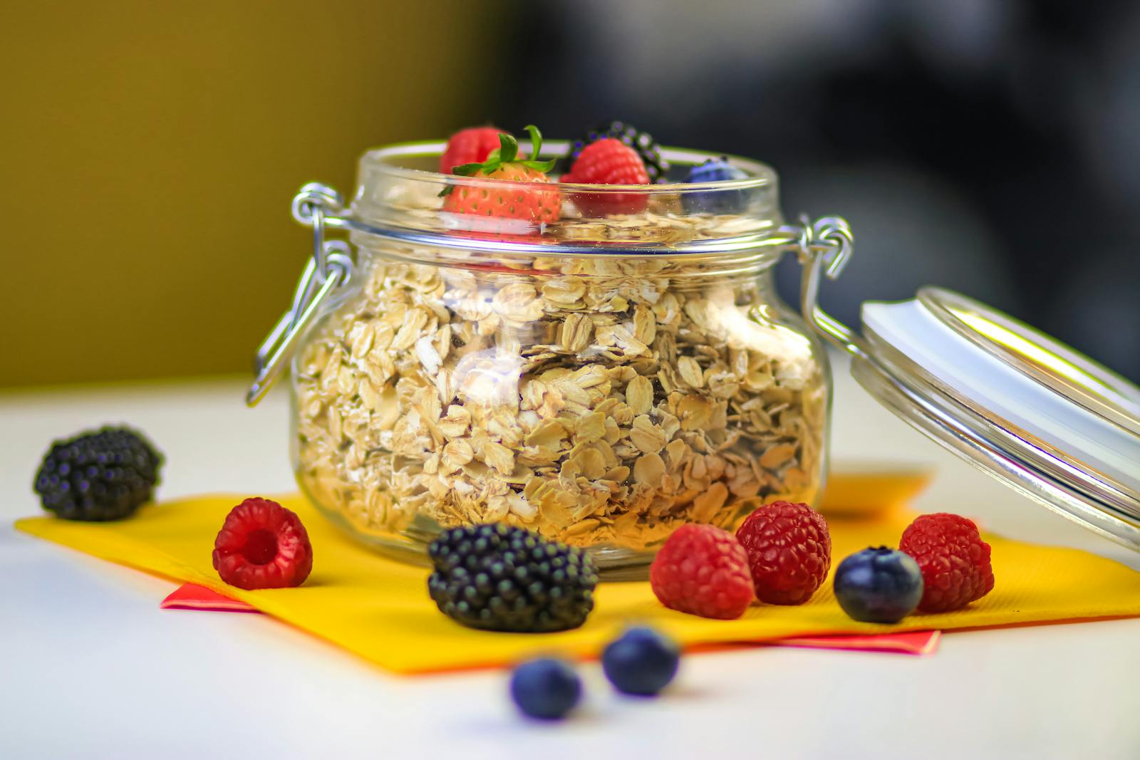 A glass jar of oats surrounded by fresh berries, the standard mise en place for a Mason-jar overnight oats setup.