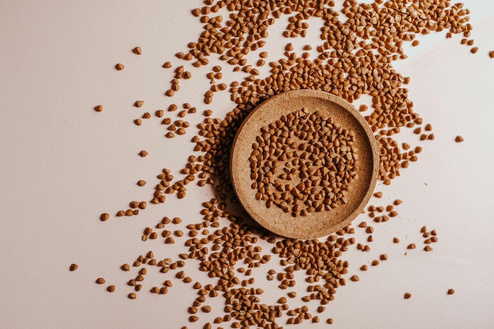 A flat lay of small triangular buckwheat groats arranged on a wooden plate, showing their distinctive pyramid shape.
