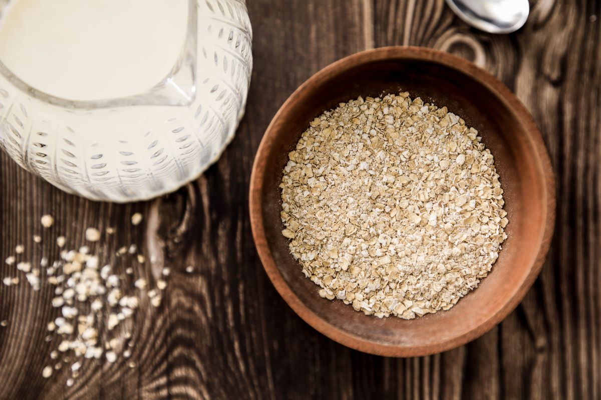 A wooden bowl of rolled oats beside a jug of milk on a rustic table.