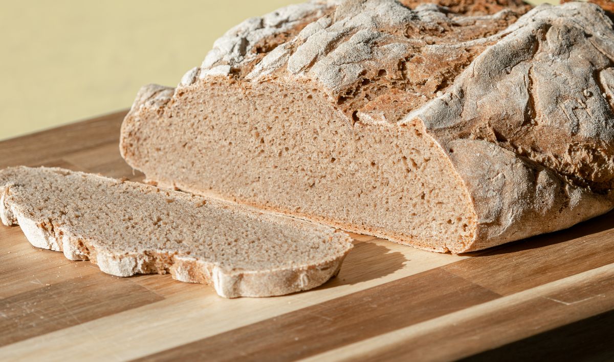 A rustic loaf of freshly baked rye bread on a wooden chopping board.