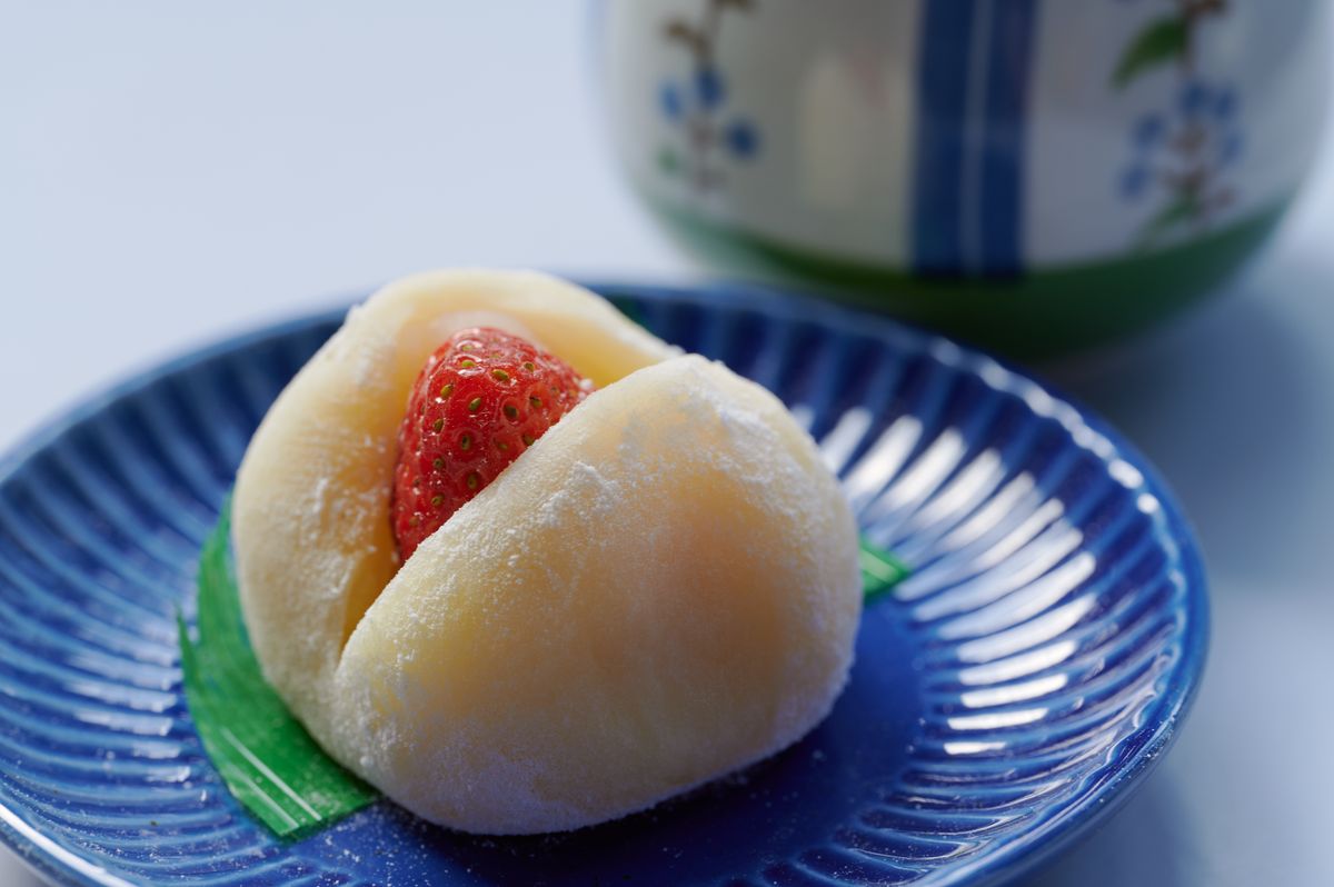 A soft white strawberry daifuku mochi split open to show the strawberry inside, on a blue ridged plate.