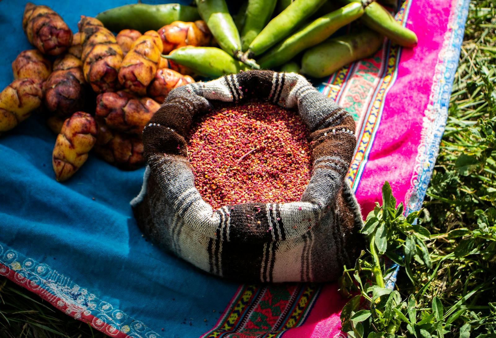 A colorful display of traditional Andean foods including quinoa, oca tubers, and beans laid out on vibrant Peruvian textiles in Tuti, Peru.