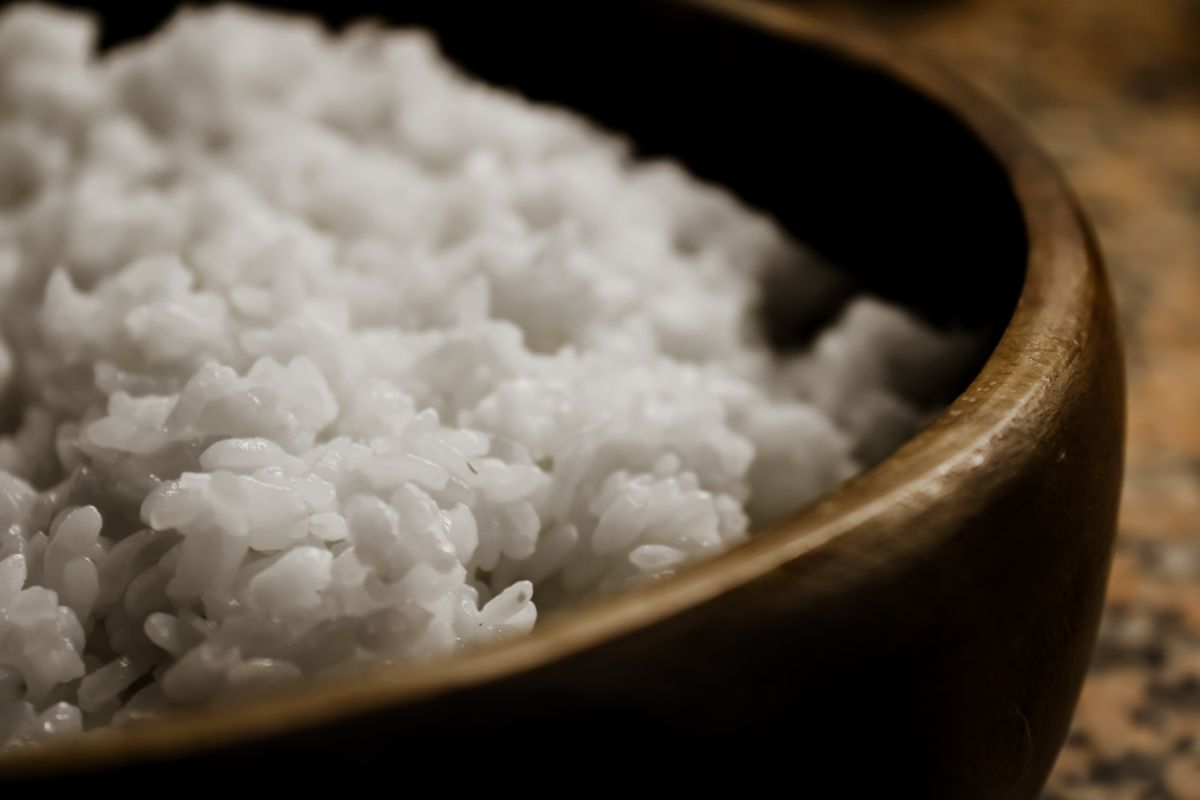 Close-up of freshly steamed white rice in a dark wooden bowl.