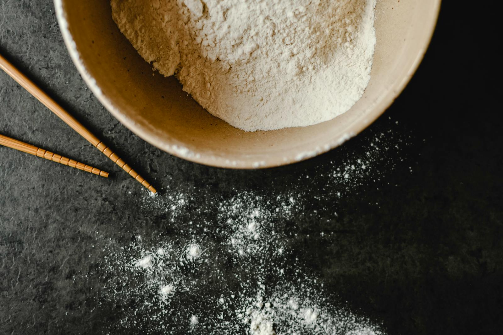A close-up of pale flour in a beige bowl on a dark background, the kind of fine-milled flour this guide is about.