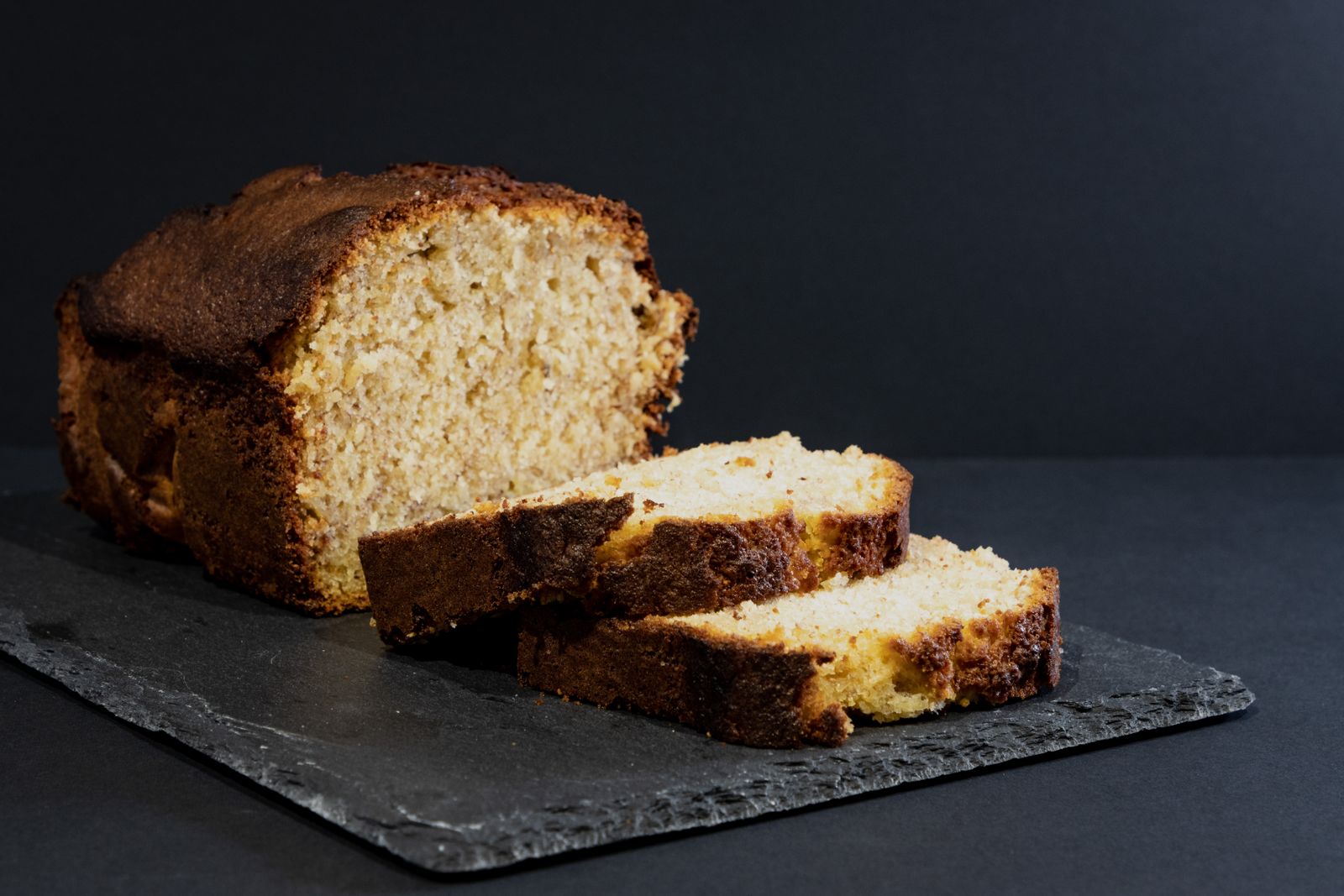 Banana bread loaf with cut slices resting on a dark slate board