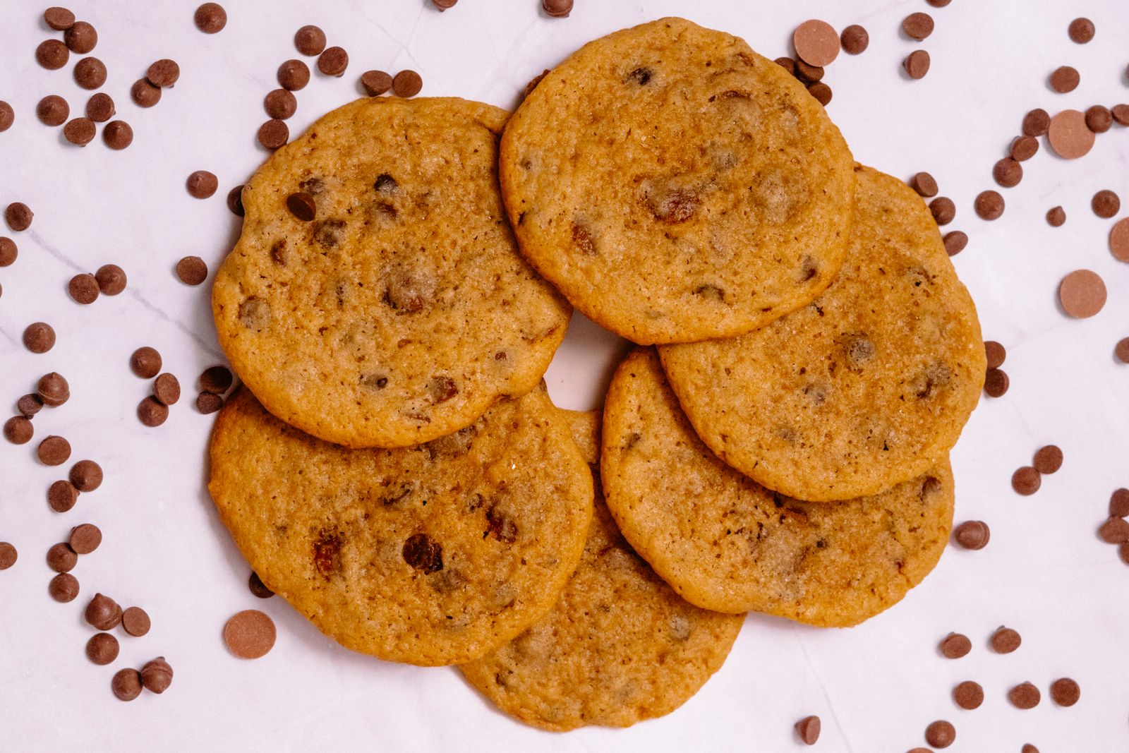 Freshly baked chocolate chip cookies surrounded by scattered chocolate chips