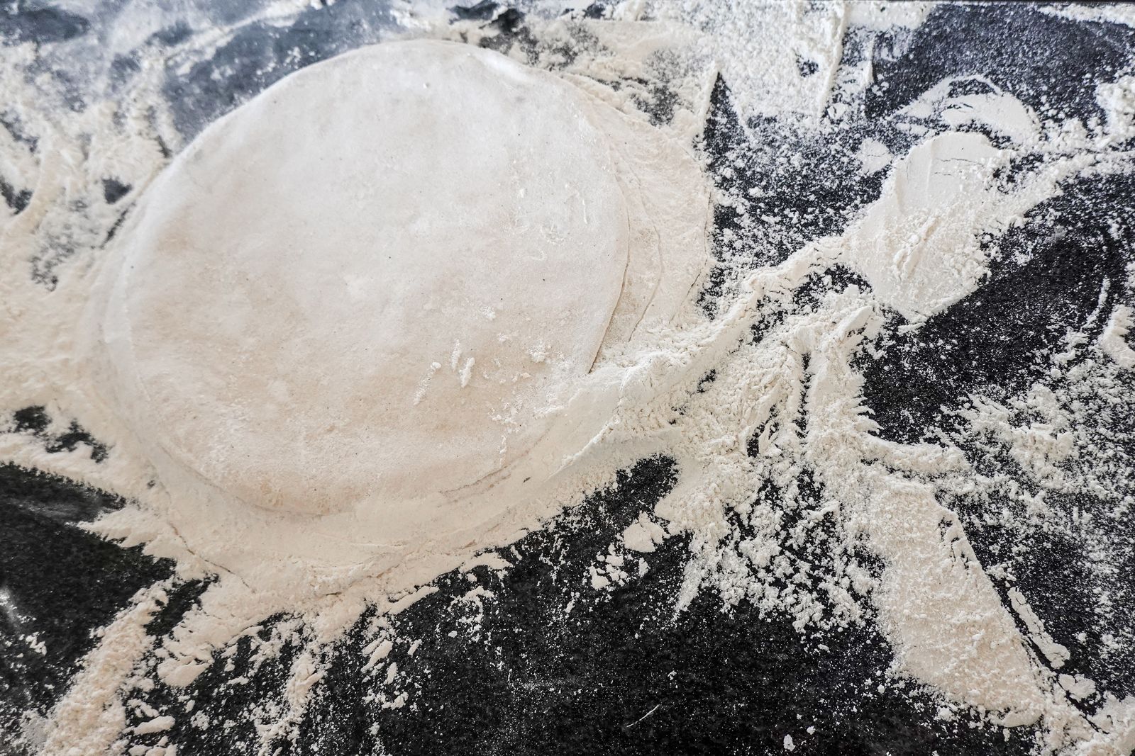 Top view of raw pizza dough on a flour-covered counter