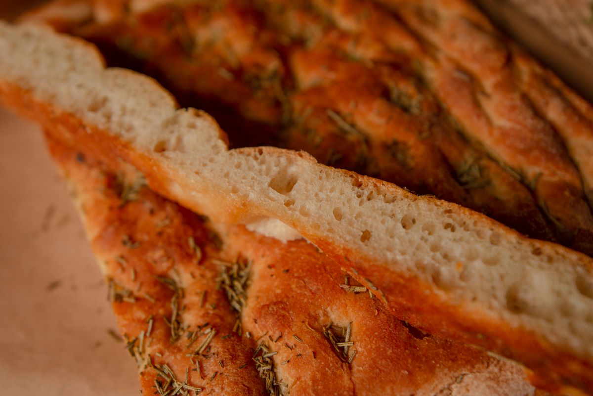 Golden sourdough focaccia scattered with rosemary, one piece cut to show the airy open crumb inside.