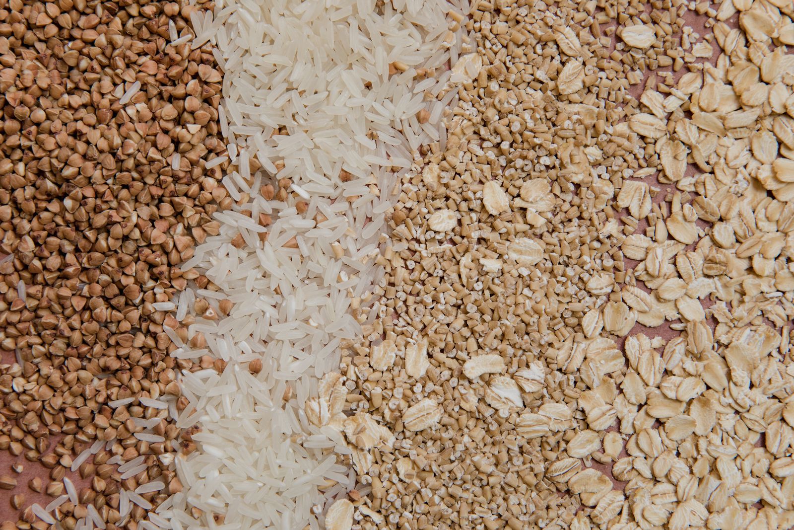 A variety of whole grains and cereals including oats, buckwheat, and rice arranged in a flat lay