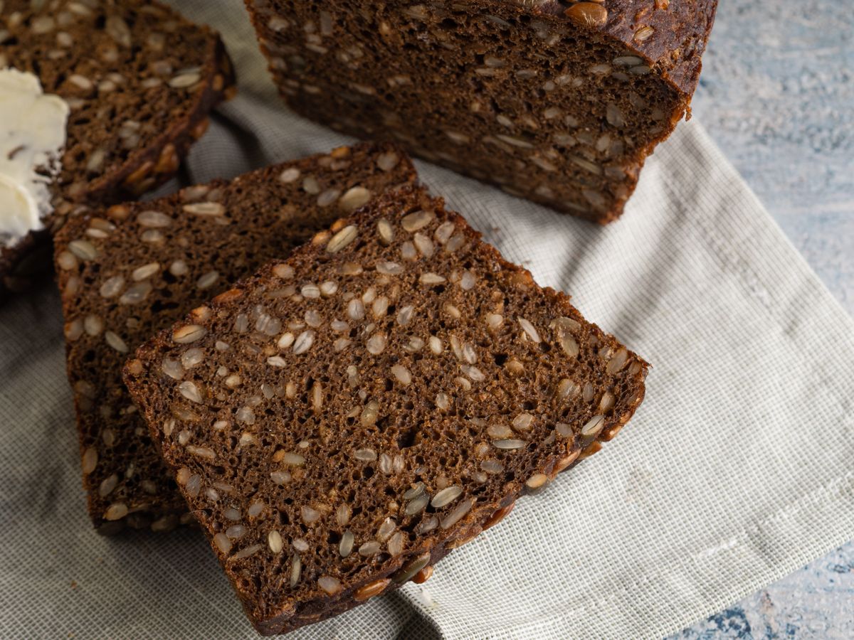 Close-up of sliced dark rye bread studded with seeds on a linen cloth.