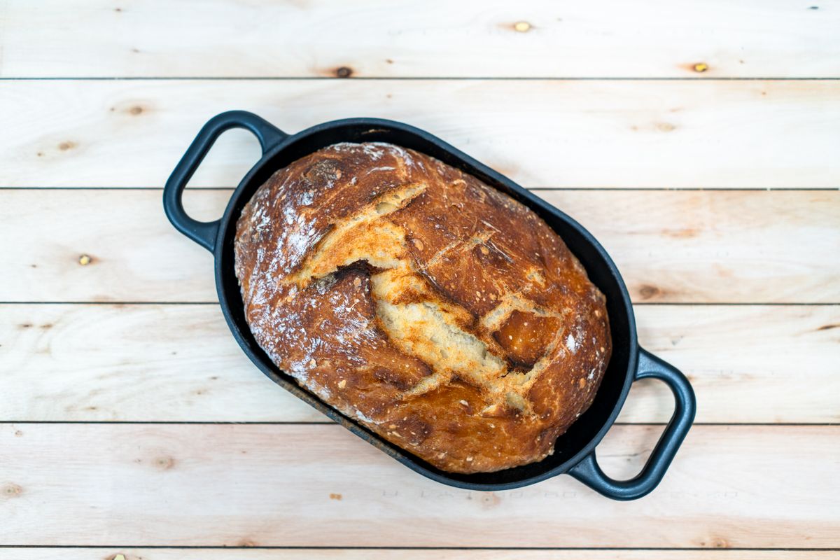 A scored sourdough loaf baked inside an oval cast-iron Dutch oven, seen from above.
