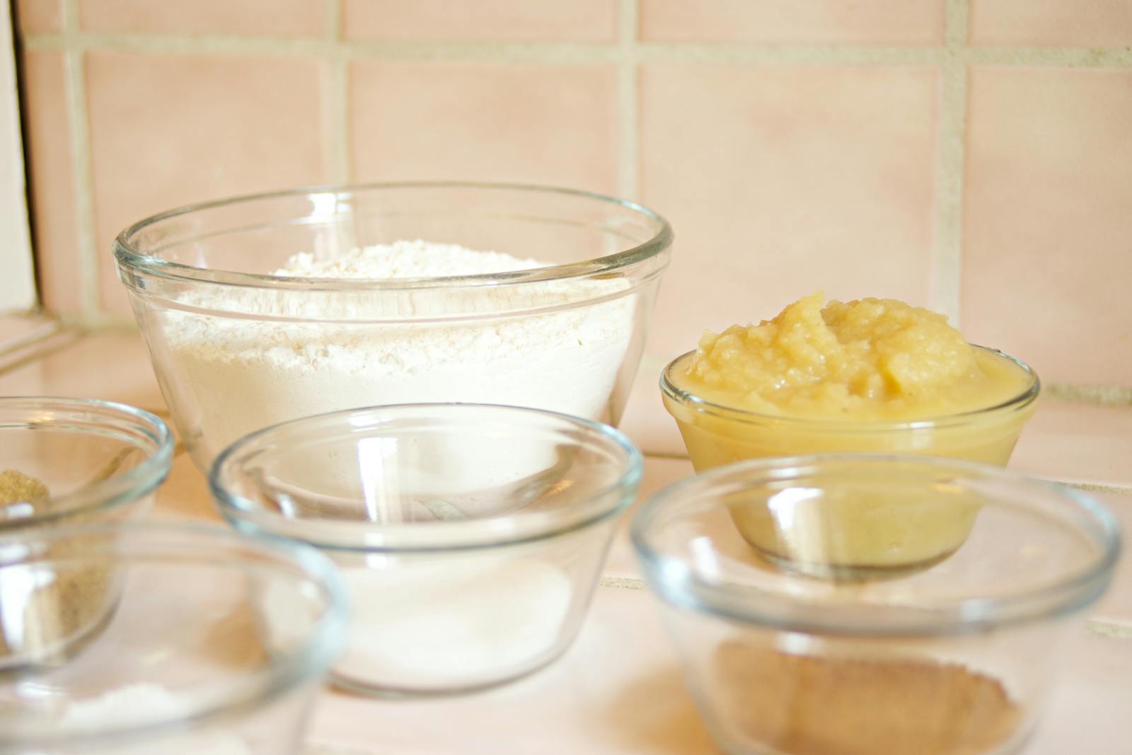 Close-up of glass bowls holding flour and other baking ingredients, set up for testing flour substitutions.