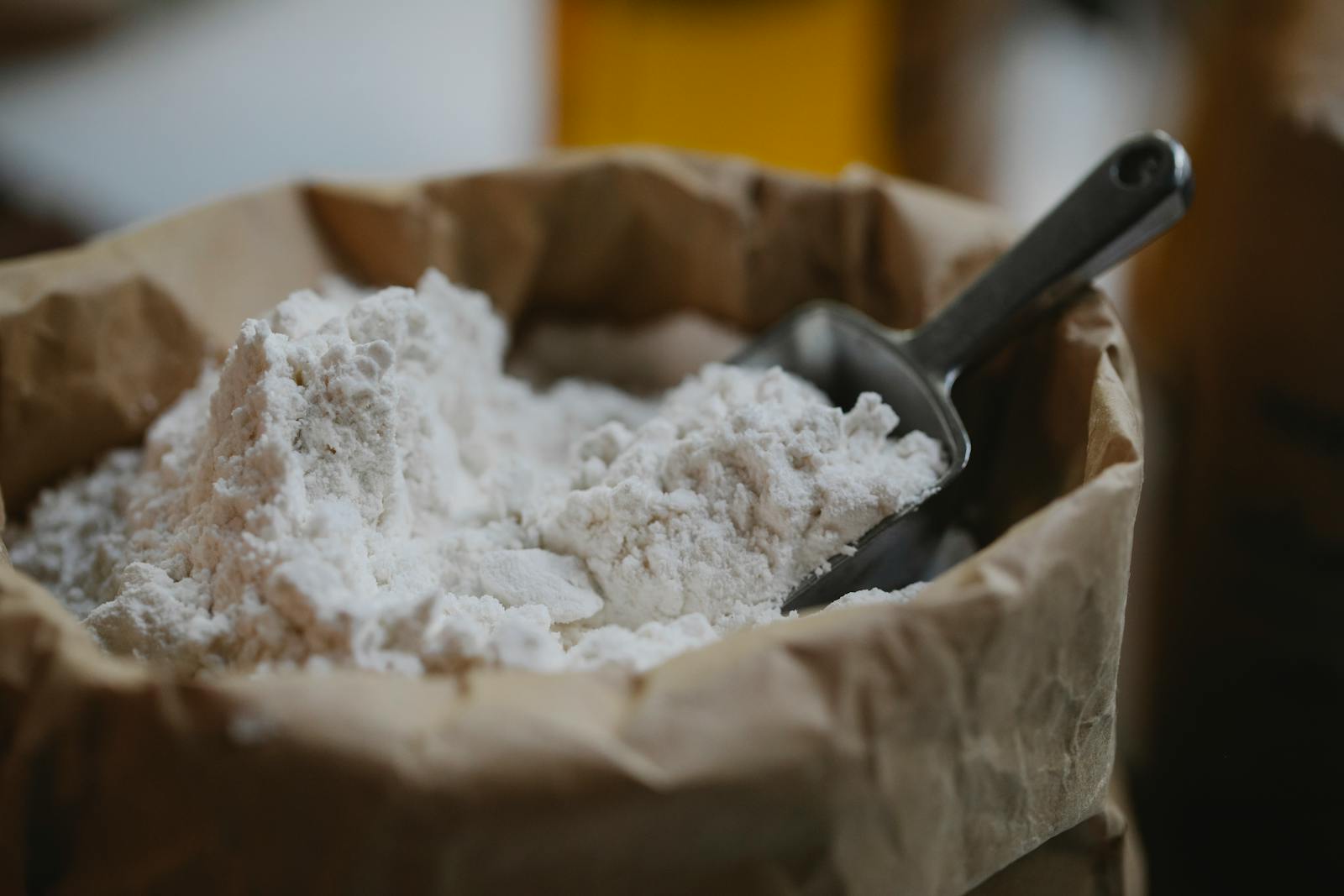 A high-angle shot of whole grain wheat flour in a bowl with a metal scoop, ready to be measured for bread.